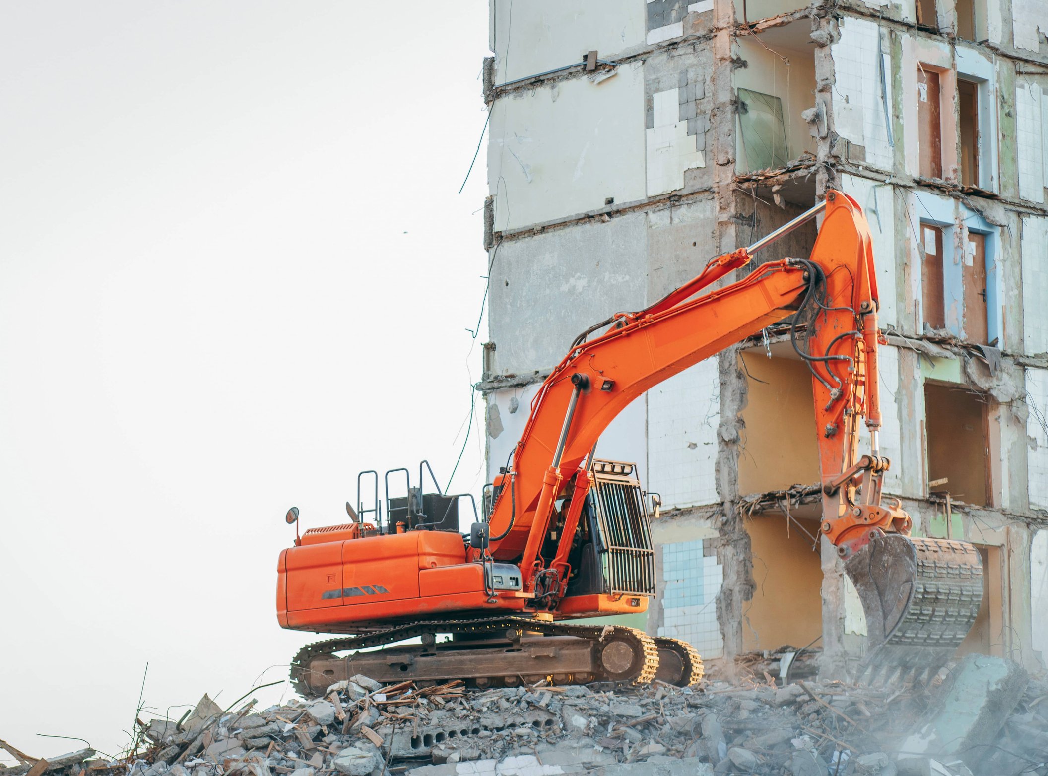 Excavator demolishing concrete building structure on rubble